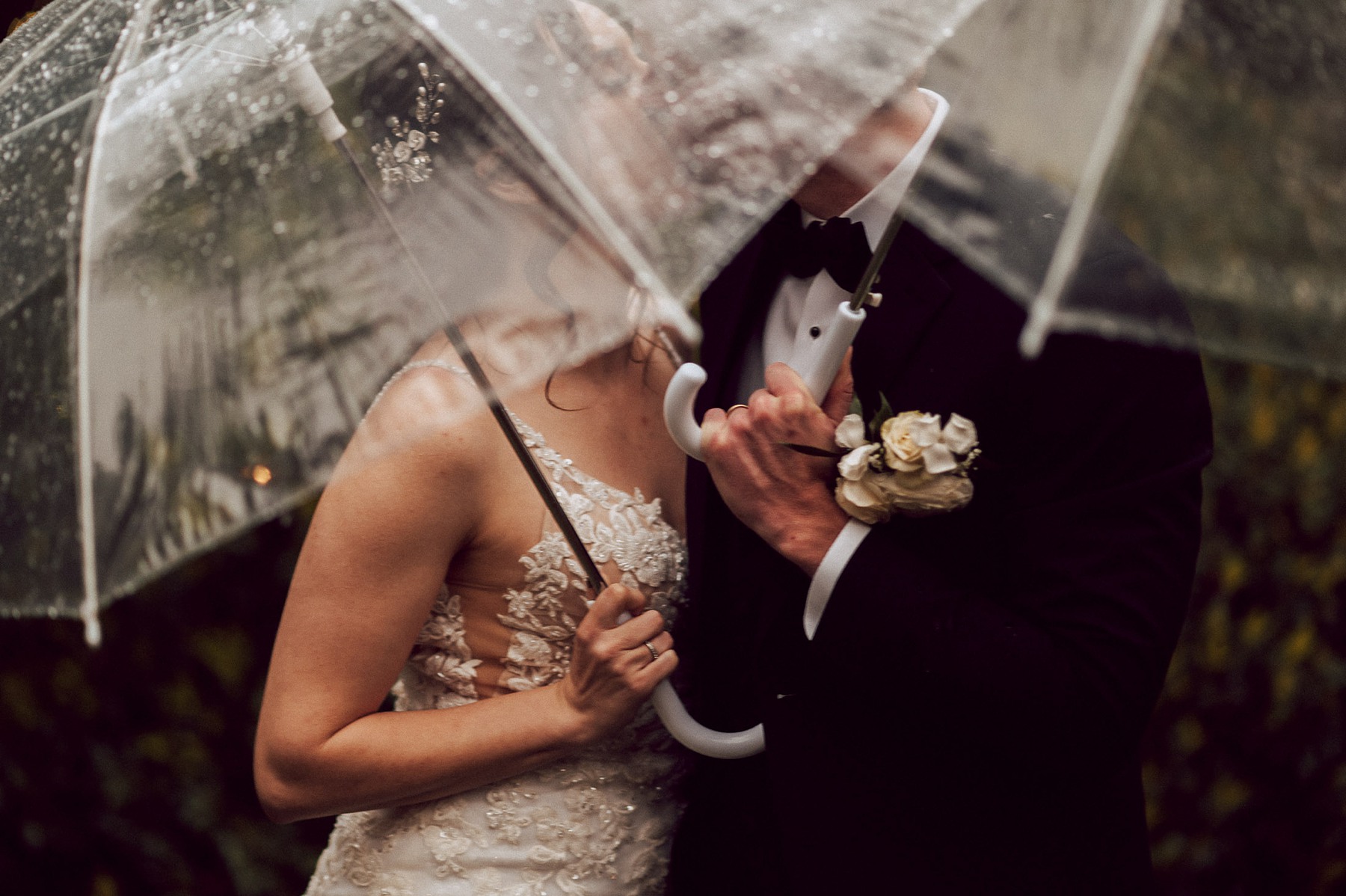 Bride and Groom kissing under clear umbrellas on rainy southern California wedding day